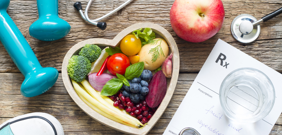 Fruits and vegetables in a heart shape container with weights and stethoscope
